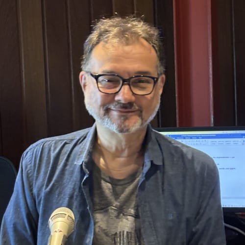 Fernando Laprieta da Flap Estúdios Fernando Laprieta, da Flap Estúdios, sentado em traje informal, em frente a um microfone, com uma tela de computador atrás dele.